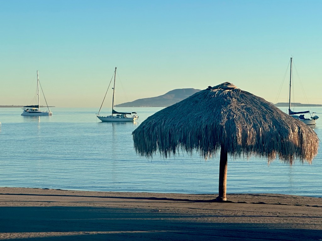 thatched beach hut with sailboats anchored behind